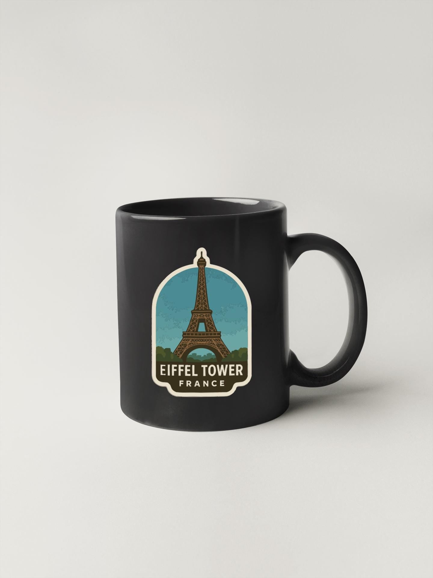 A black coffee mug with a graphic of the Eiffel Tower and the text "Eiffel Tower France" printed on it.