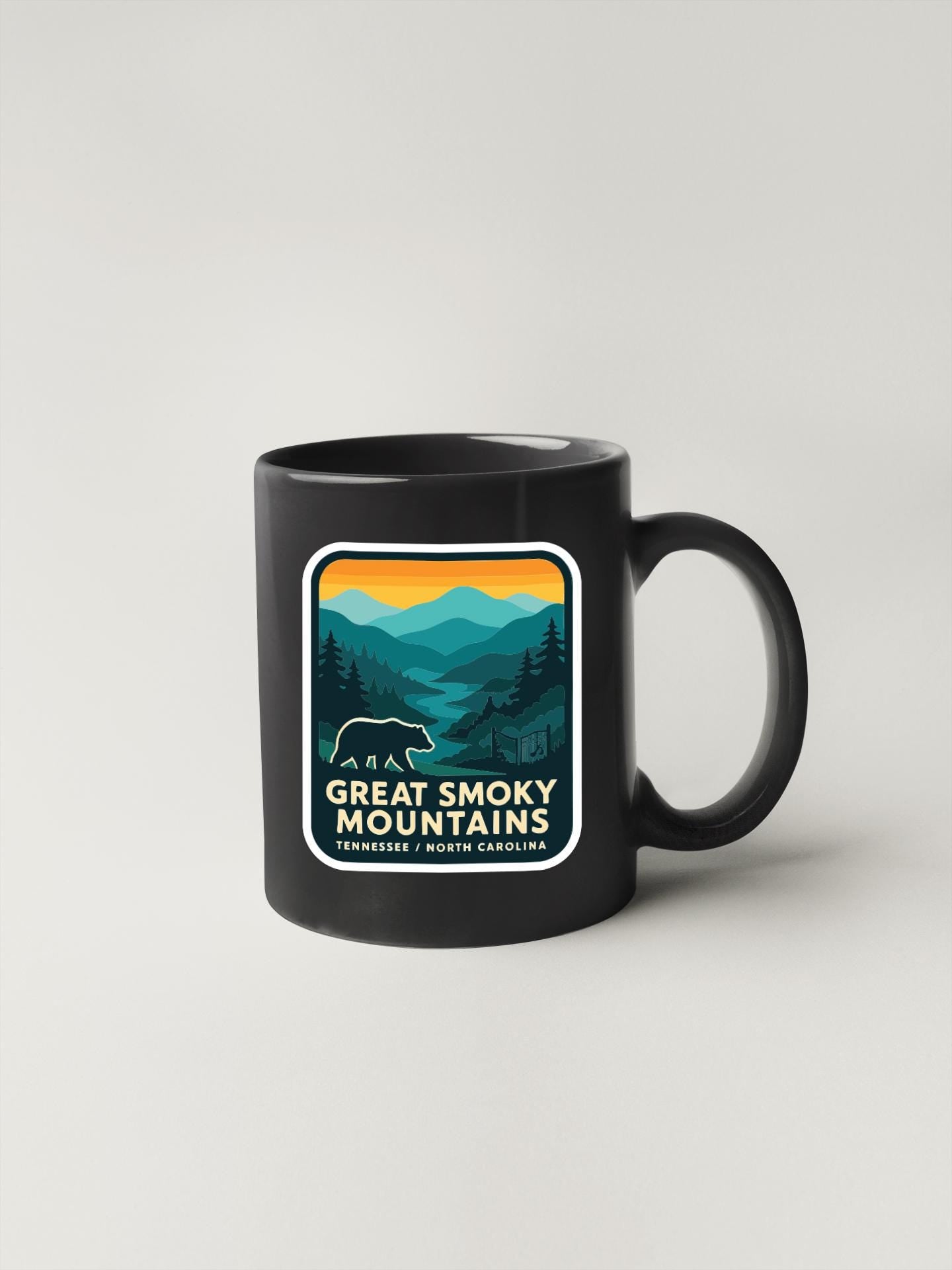 A black coffee mug with a graphic design depicting a mountain landscape and a bear.