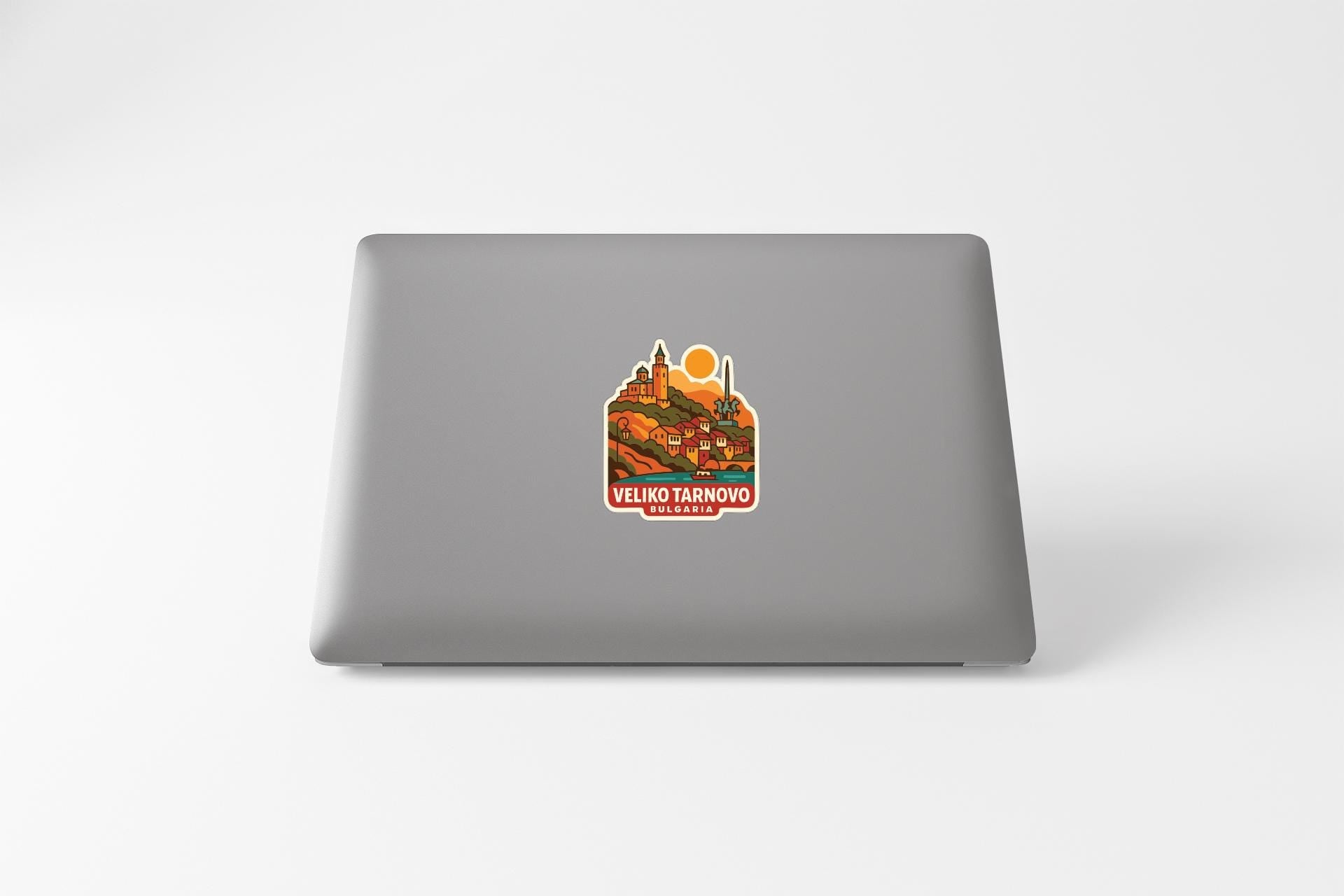 a sticker on the back of a laptop, depicting a scenic landscape with a castle and a sun.