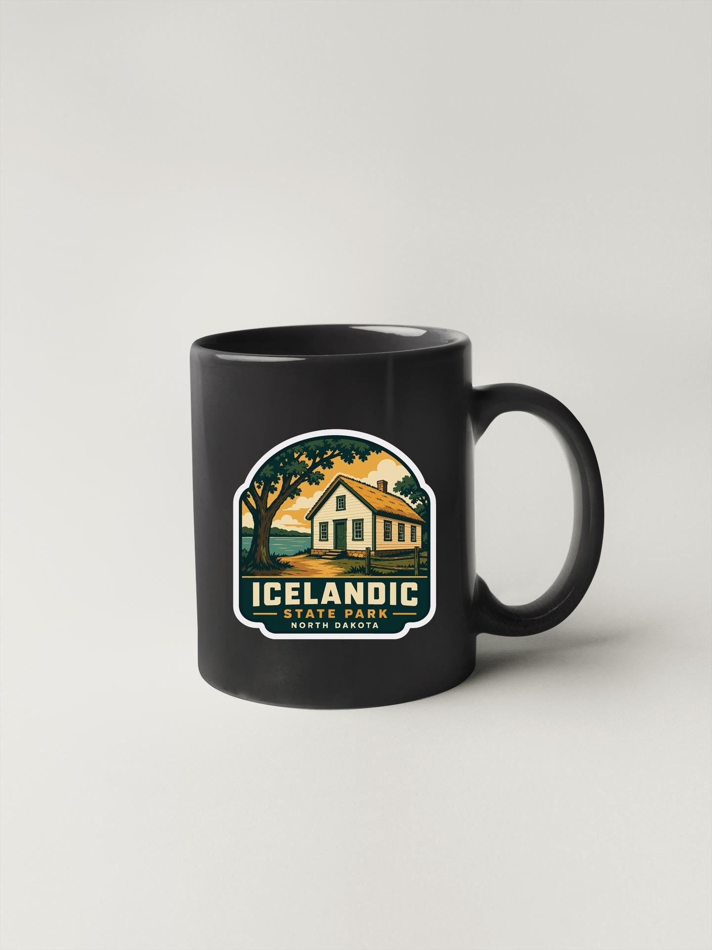 A black coffee mug with a graphic design depicting a house and trees, along with the text "Icelandic State Park North Central".
