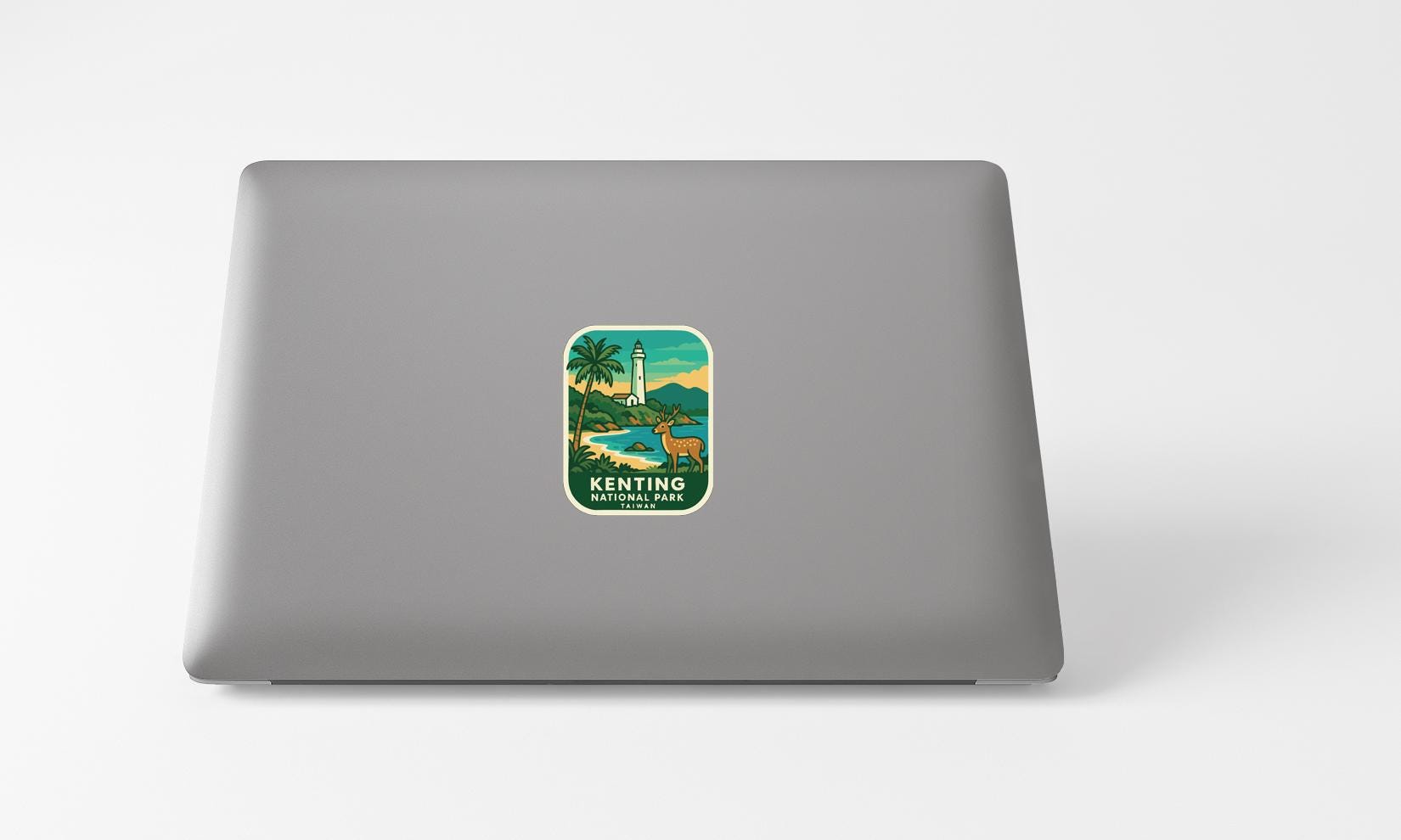 A sticker on the back of a laptop, depicting a tropical landscape with a lighthouse and palm trees.
