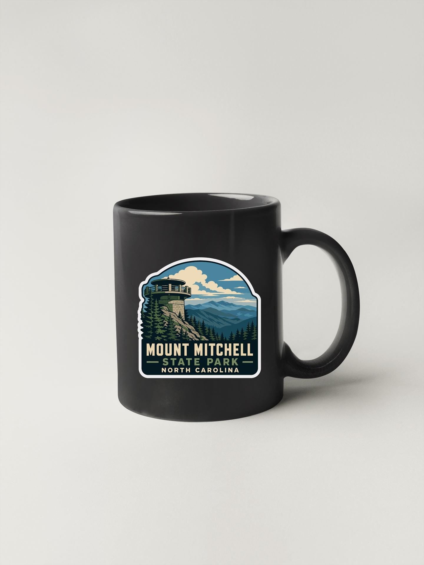A black coffee mug with a graphic design depicting Mount Mitchell State Park in North Carolina.