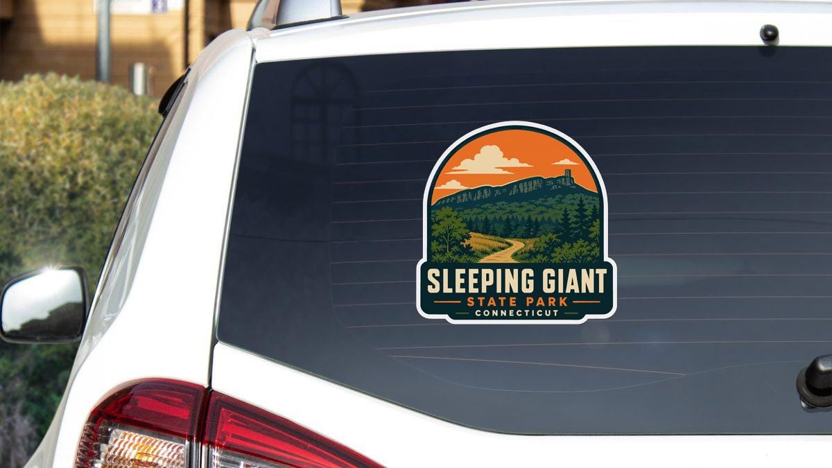 a sticker on the rear window of a white vehicle, depicting a scenic mountain landscape with a winding road and a cloudy sky.