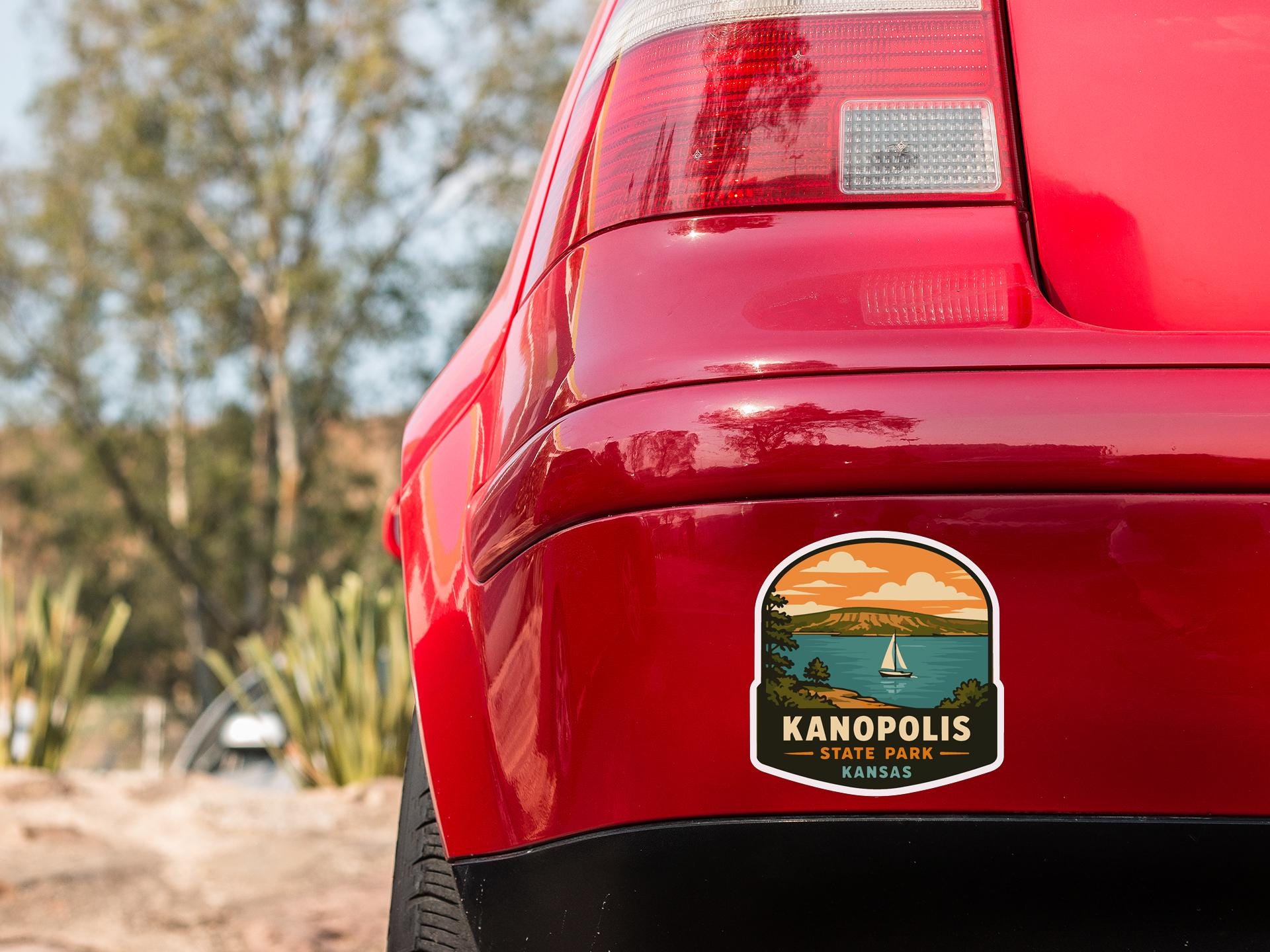 the rear end of a red car with a sticker on the back window that says "Kanopolis State Park Kansas".