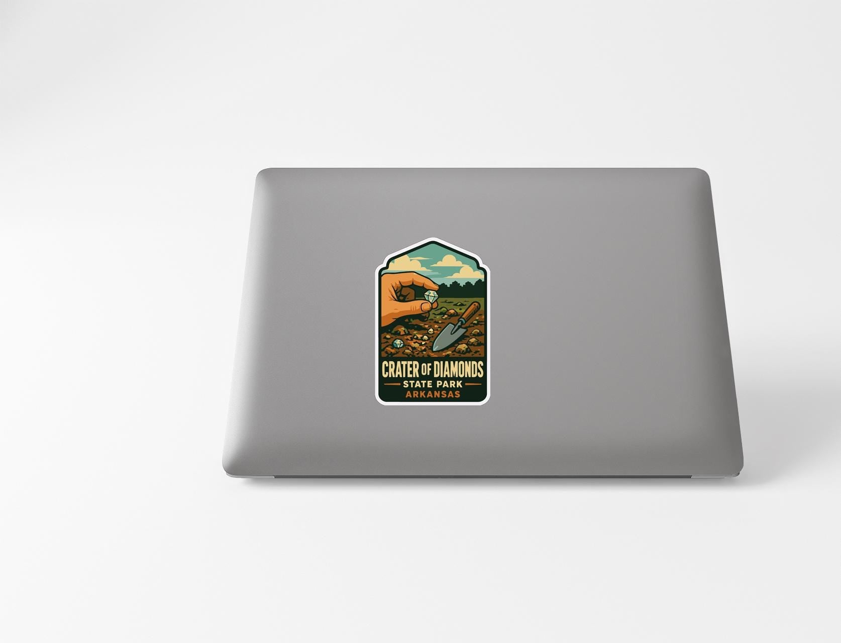 a sticker on a laptop with a vintage-style illustration of a hand holding a magnifying glass over a field of flowers.
