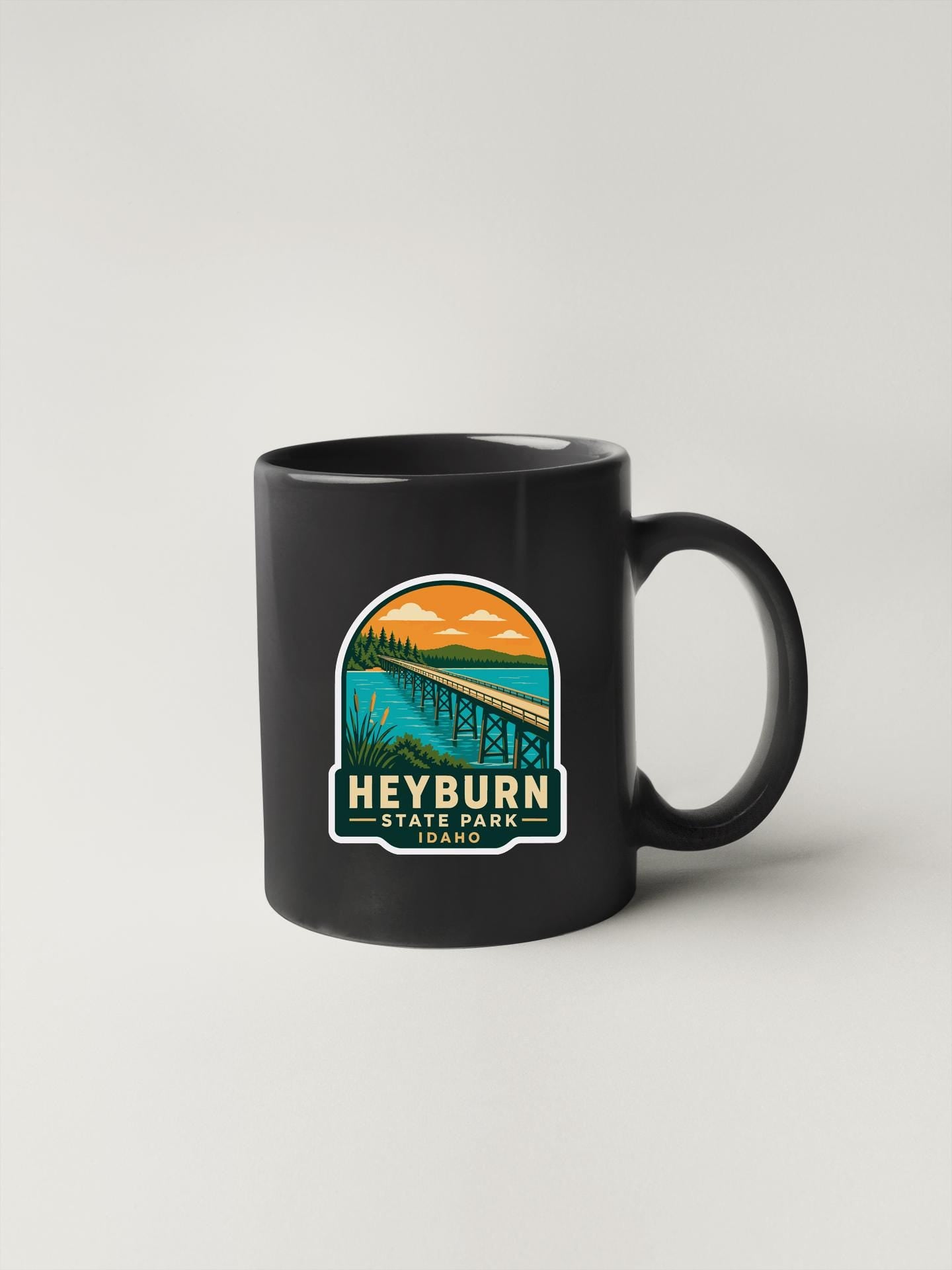A black coffee mug with a colorful graphic design depicting a bridge and a scenic landscape.
