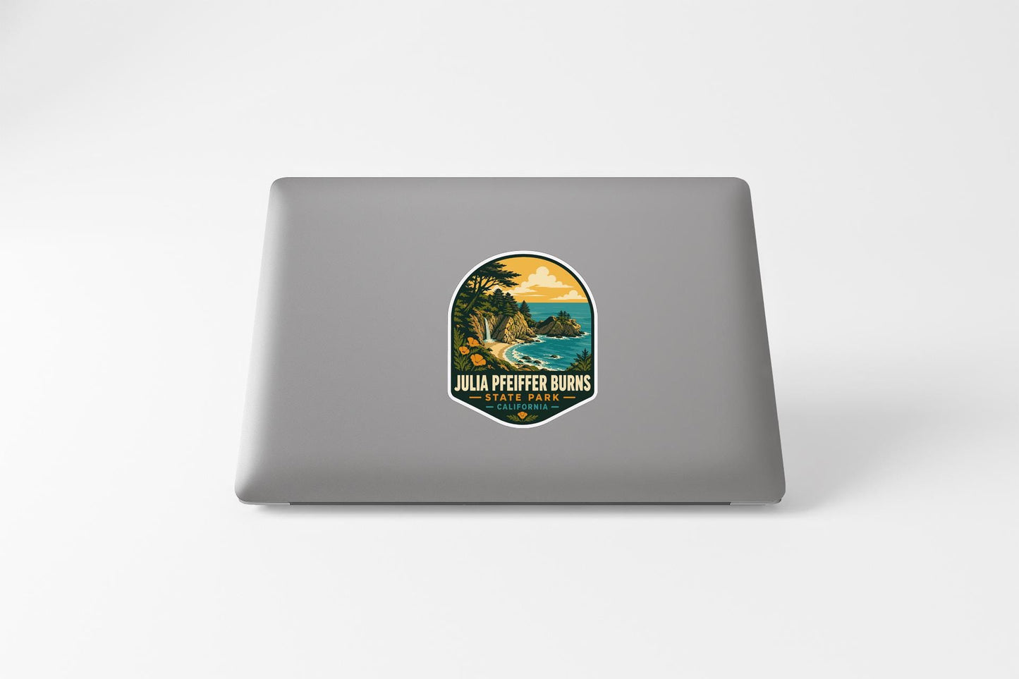 A sticker on the back of a laptop, depicting a scenic landscape with a beach and mountains.