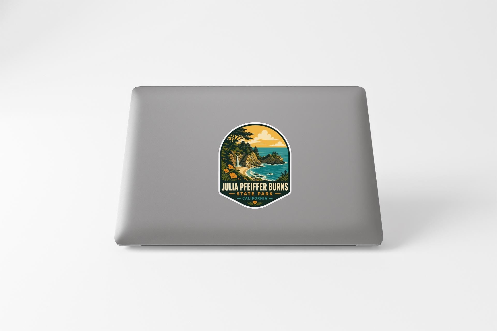 A sticker on the back of a laptop, depicting a scenic landscape with a beach and mountains.