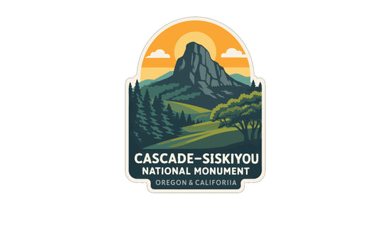 a sticker or emblem with a mountain landscape and a sun in the sky. The text below the image reads "CASCADE-SISKiyOU NATIONAL MONUMENT OREGON & CALIFORNIA".