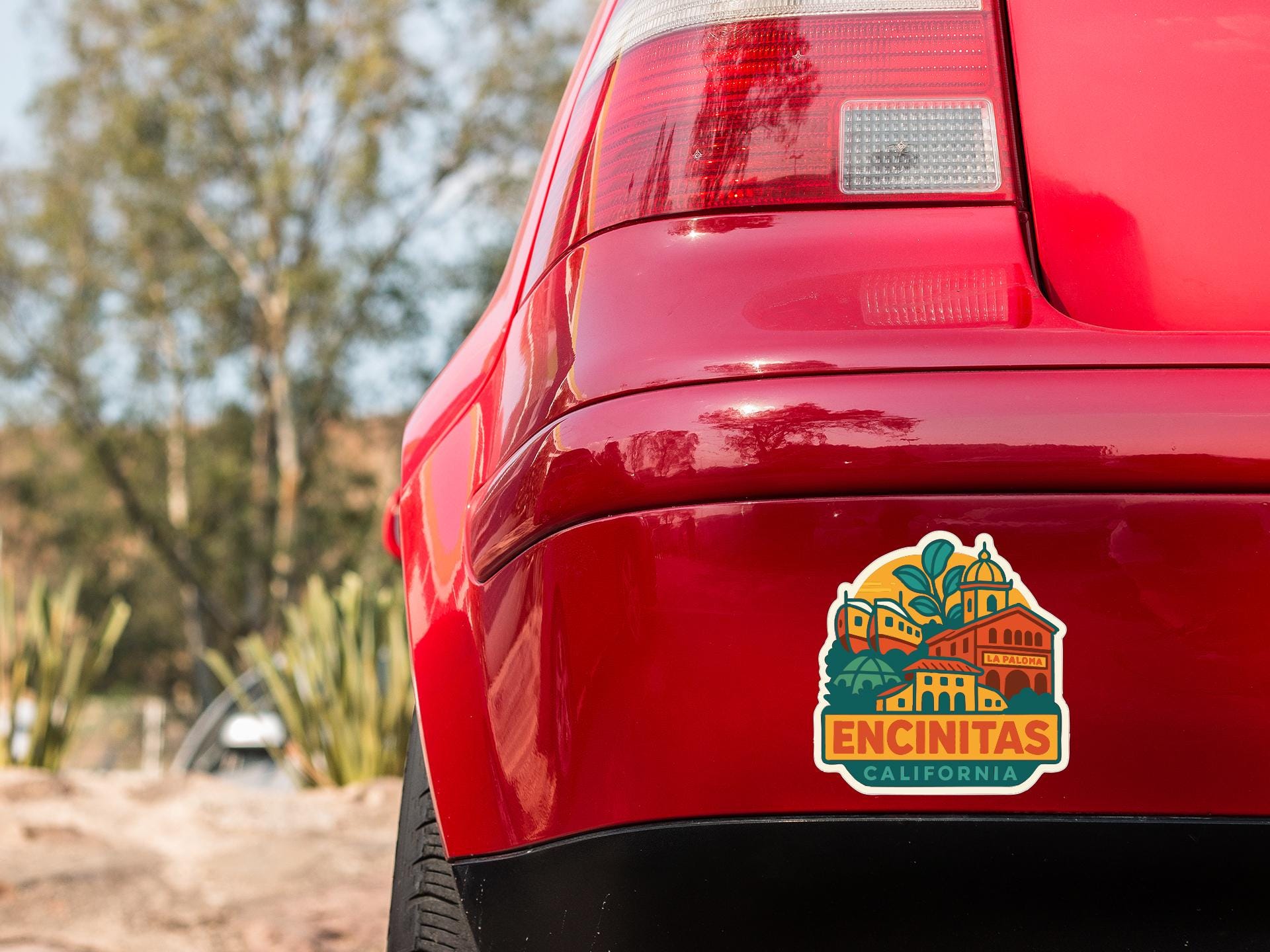 the rear end of a red car with a sticker on the trunk that says "ENCINITAS, CALIFORNIA".