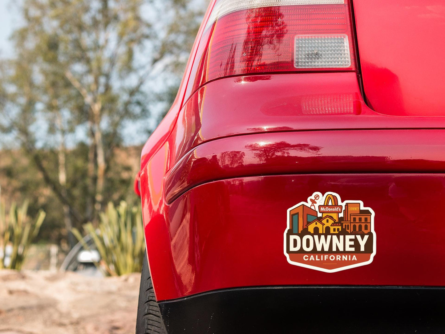 the rear end of a red car with a sticker on the back window that says "DOWNEY, CALIFORNIA".
