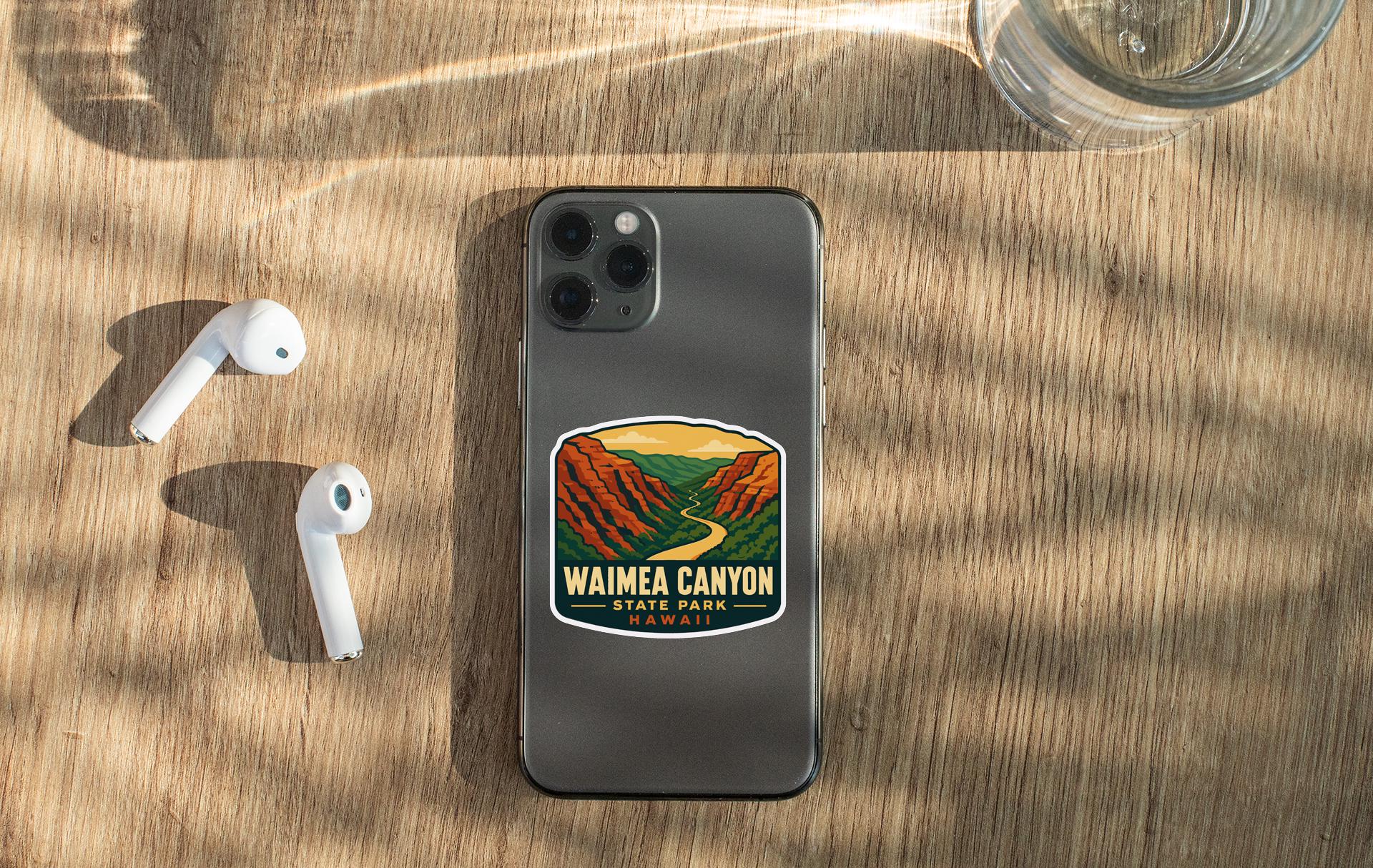 a smartphone with a sticker of Waimea Canyon on it, along with a pair of white earbuds and a glass of water on a wooden surface.