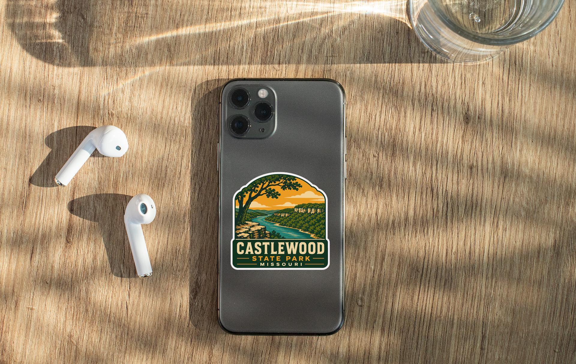 a smartphone with a sticker on it, placed on a wooden surface alongside a pair of white earbuds and a glass of water.
