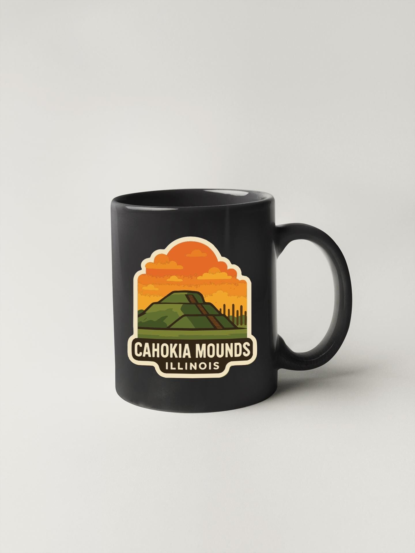 A black coffee mug with a graphic design depicting a mountain landscape and the text "CAHOKIA MOUNDS ILLINOIS".