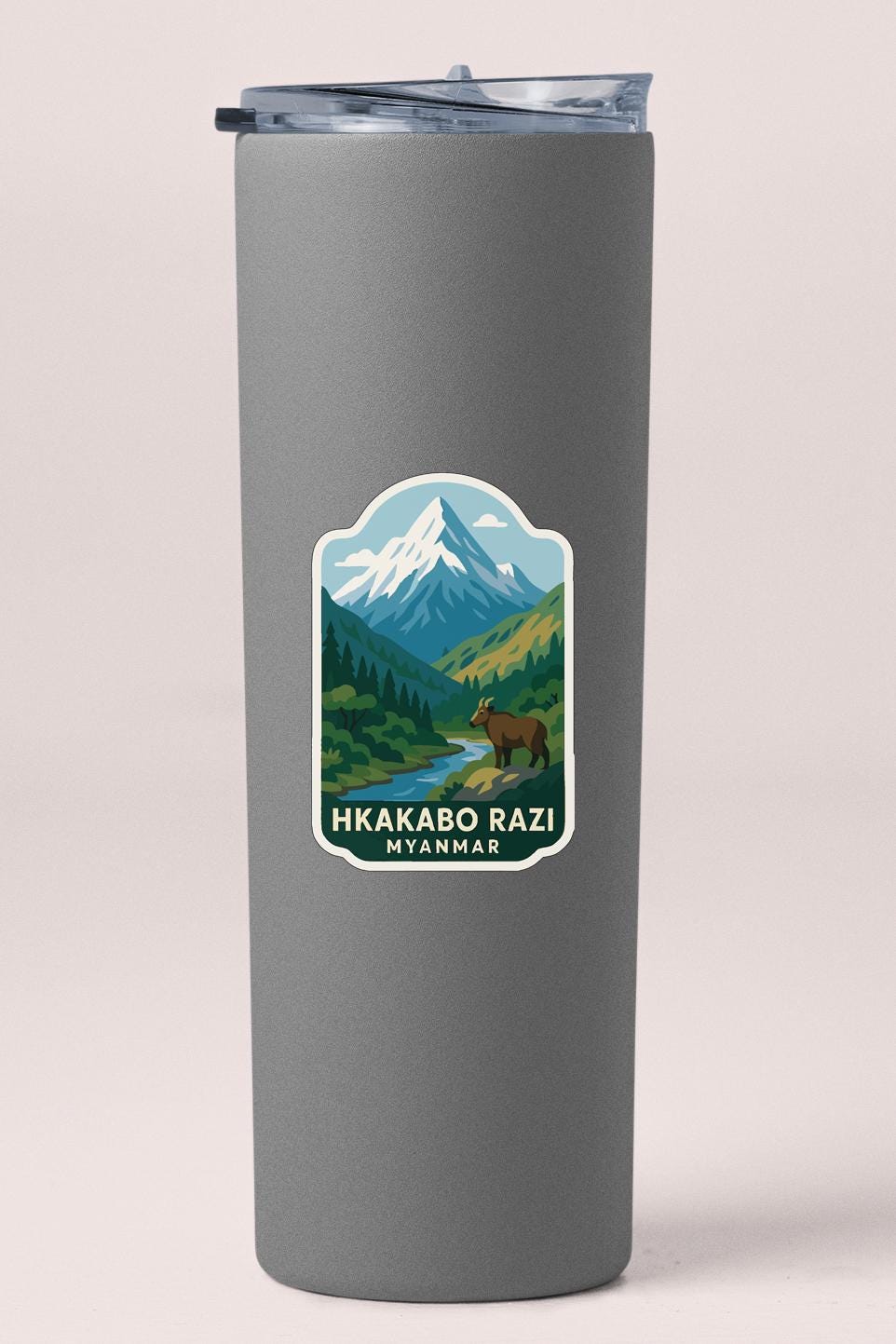 A gray tumbler with a sticker depicting a mountain landscape and a bear.