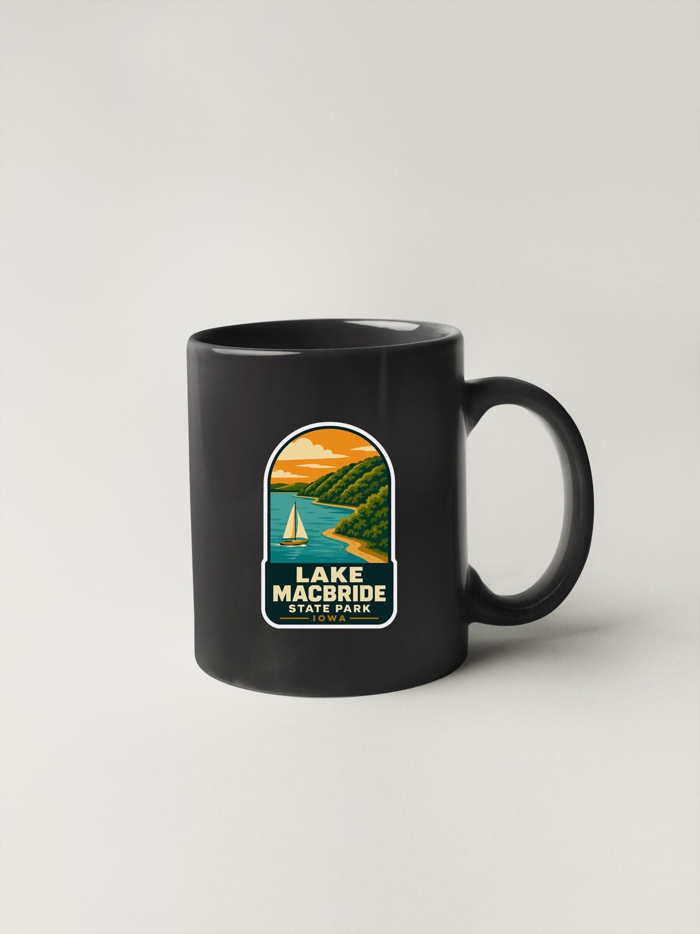 A black coffee mug with a graphic design depicting Lake Macbride State Park.