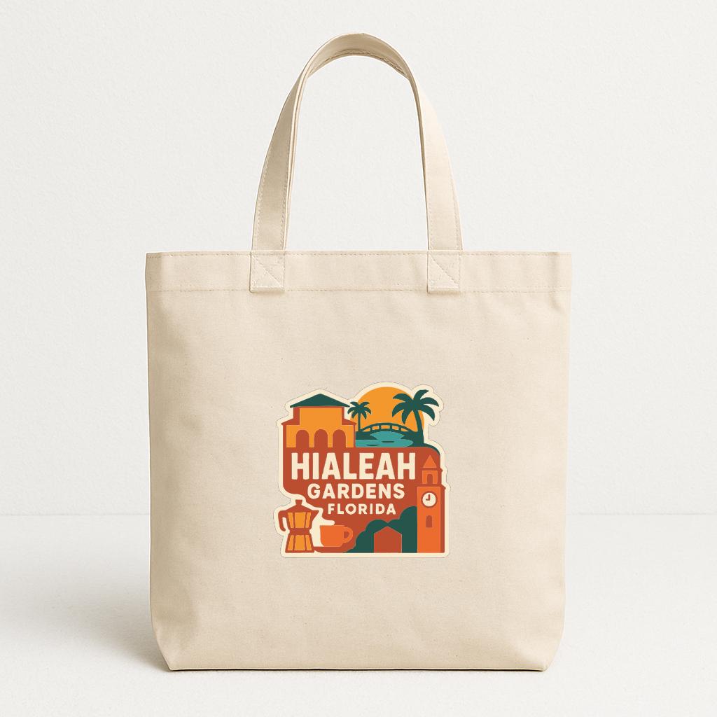 A beige tote bag with a graphic design featuring a tropical scene with palm trees, a building, and a clock.