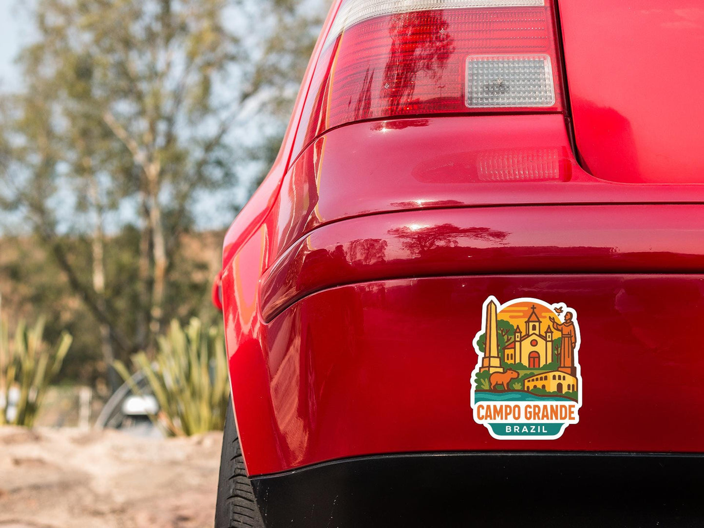 the rear end of a red car with a sticker on it, featuring a colorful illustration of a building and trees.