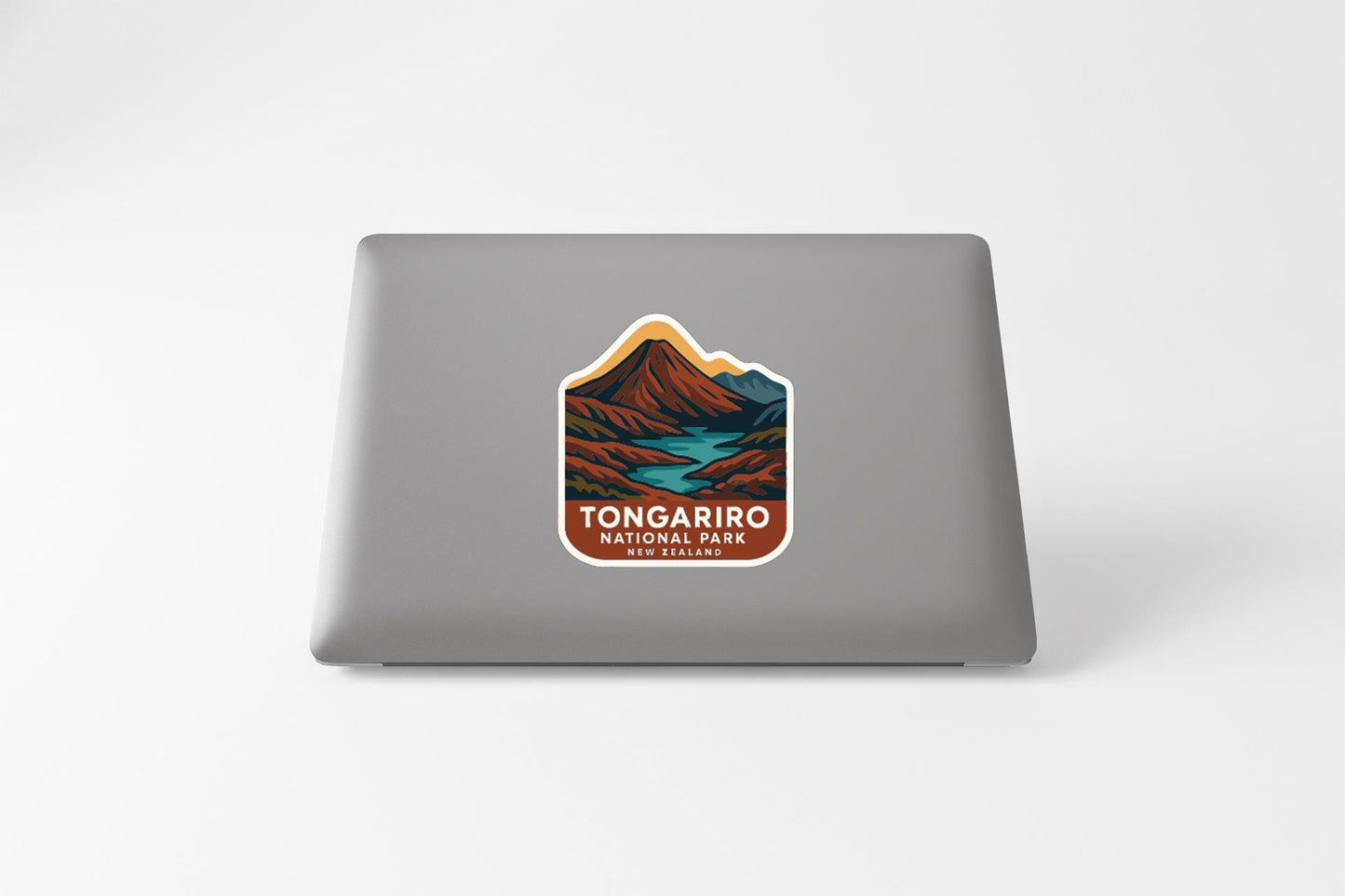 a sticker or decal on the back of a laptop, depicting a mountain landscape with a river or stream running through it. The sticker has the text "Tongaariro National Park" written on it, indicating that the laptop is likely used for work or travel related to this national park.