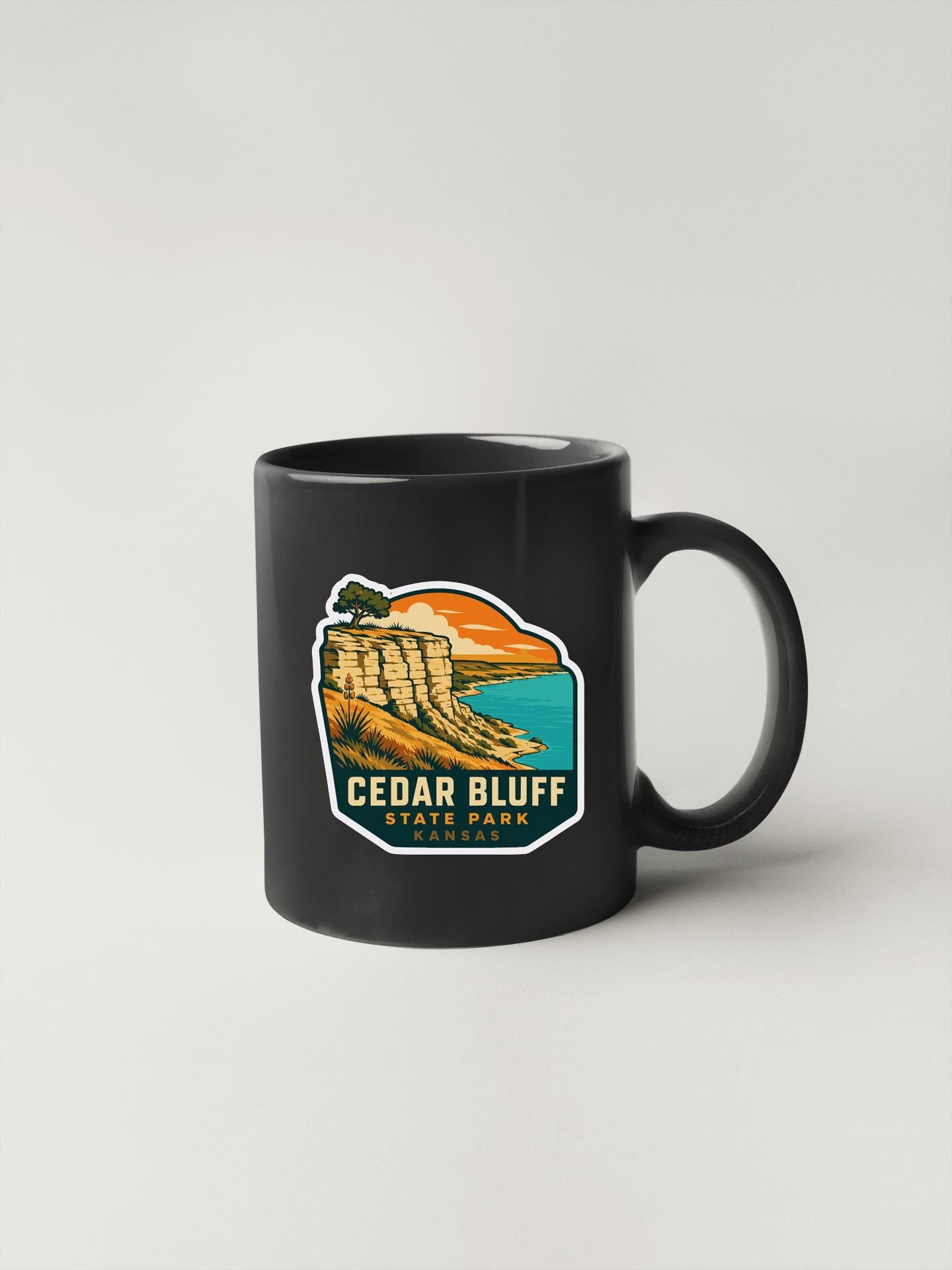 A black coffee mug with a graphic design depicting a scenic landscape with a cliff, beach, and sunset.