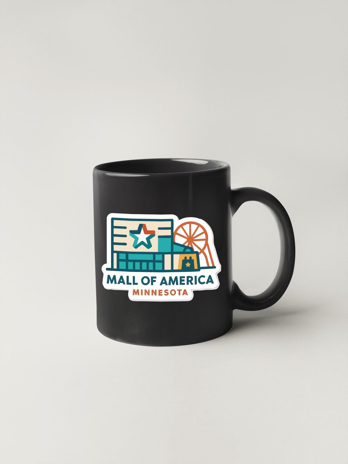 A black coffee mug with a colorful graphic depicting a mall and a ferris wheel, along with the text "MALL OF AMERICA MINNESOTA".