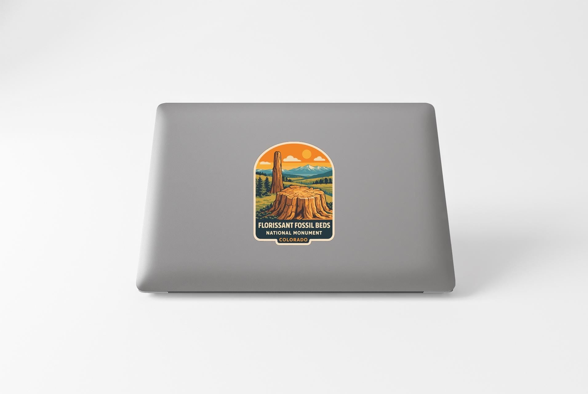 A sticker on the back of a laptop, depicting a fossilized tree stump and mountains in the background.