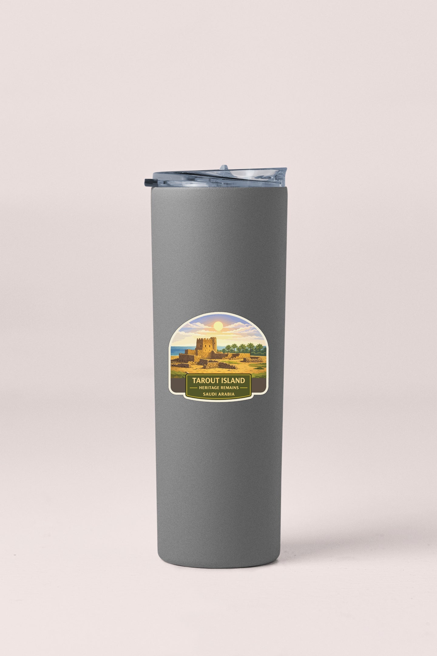 A gray insulated tumbler with a label that reads "TAROUT ISLAND SAUDIA" and features a scenic illustration of a castle and landscape.