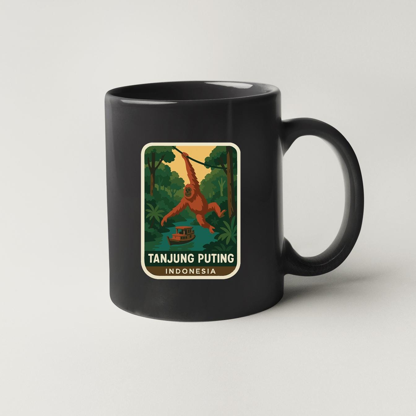 A black coffee mug with a sticker depicting an orangutan swinging through a jungle scene, along with the text "TANJUNG PUTING INDONESIA".