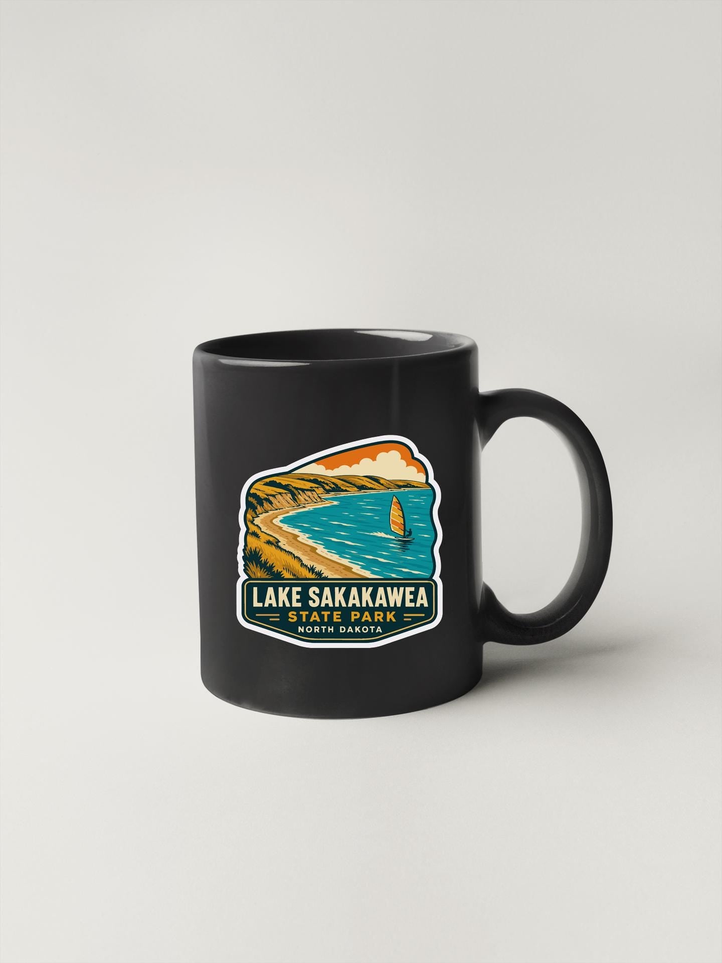 A black coffee mug with a printed design depicting Lake Sakakawea State Park in the United States.