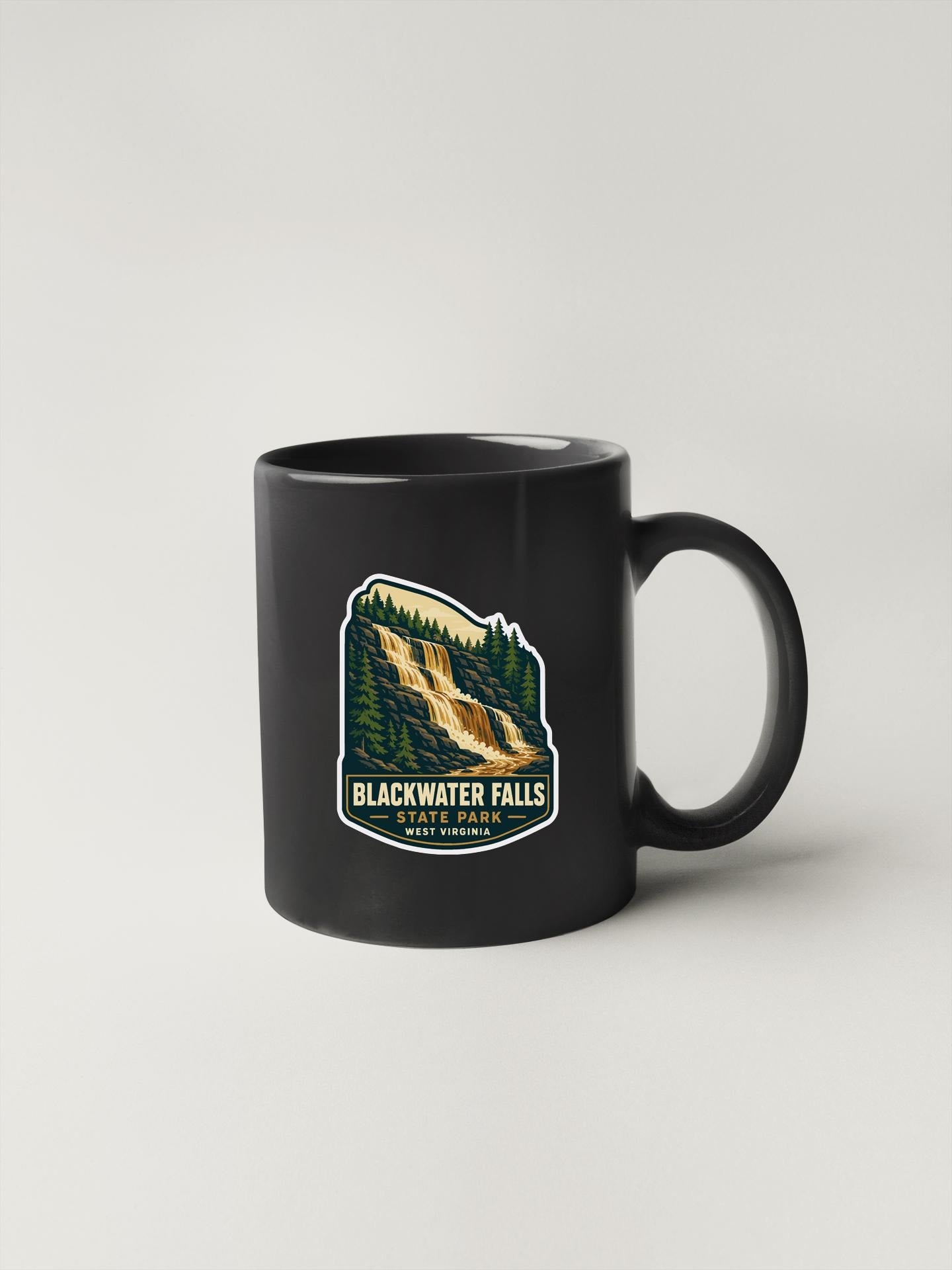A black coffee mug with a graphic design depicting Blackwater Falls, a waterfall surrounded by trees, and the text "Blackwater Falls State Park West Virginia".