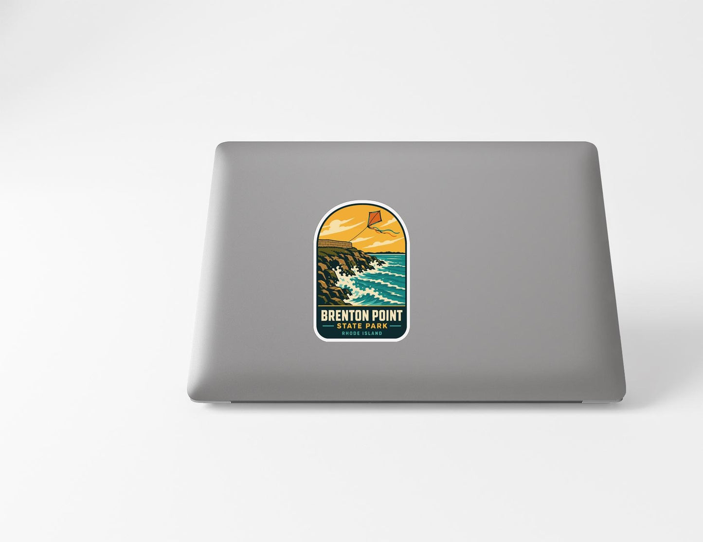 A sticker on the back of a laptop, depicting a scenic coastal landscape with mountains, water, and a kite flying in the sky.
