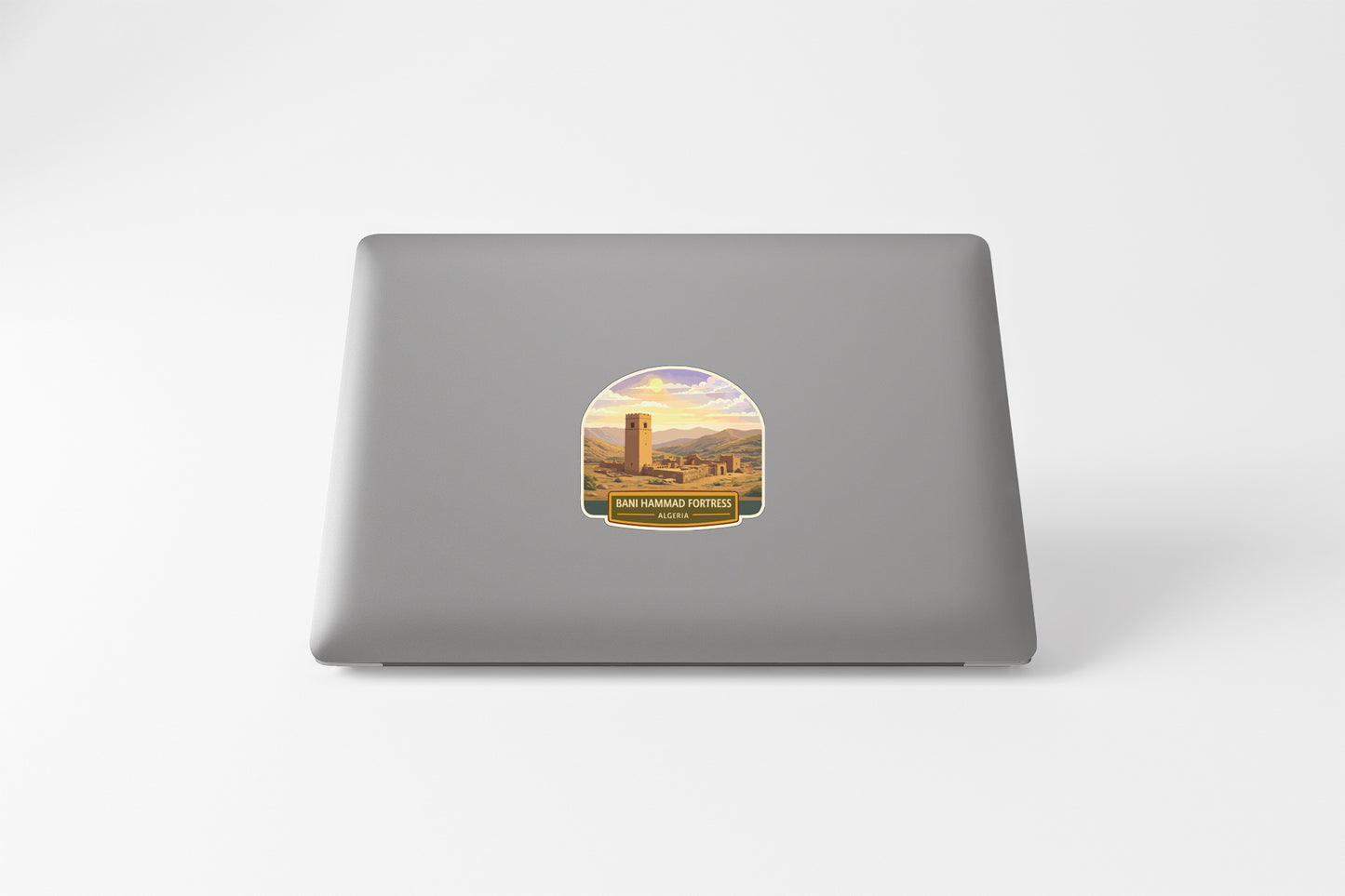 a sticker on the back of a laptop, depicting a scenic landscape with mountains and a tower in the distance.