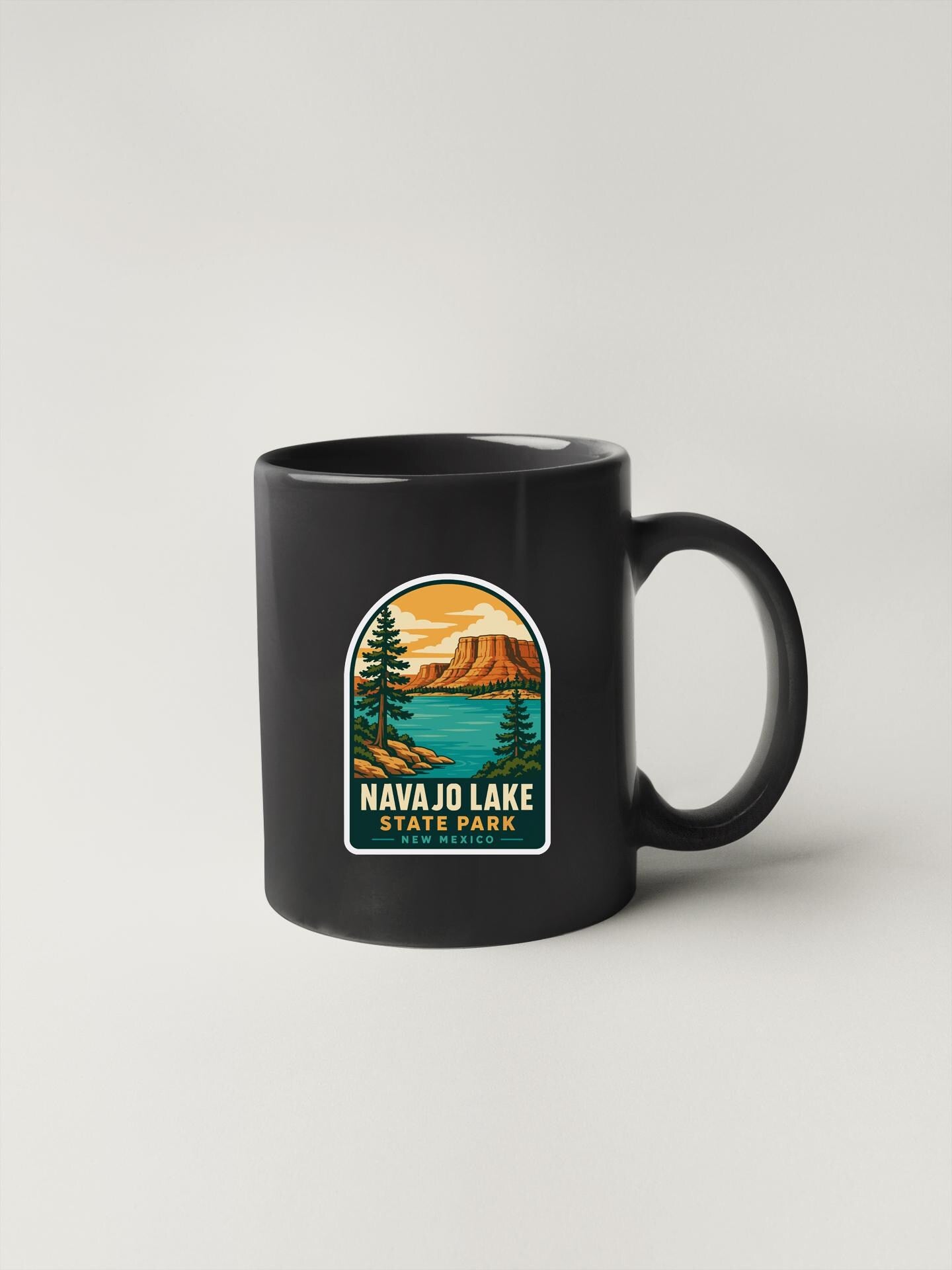 A black coffee mug with a graphic design depicting a scenic landscape featuring a lake, mountains, and pine trees.