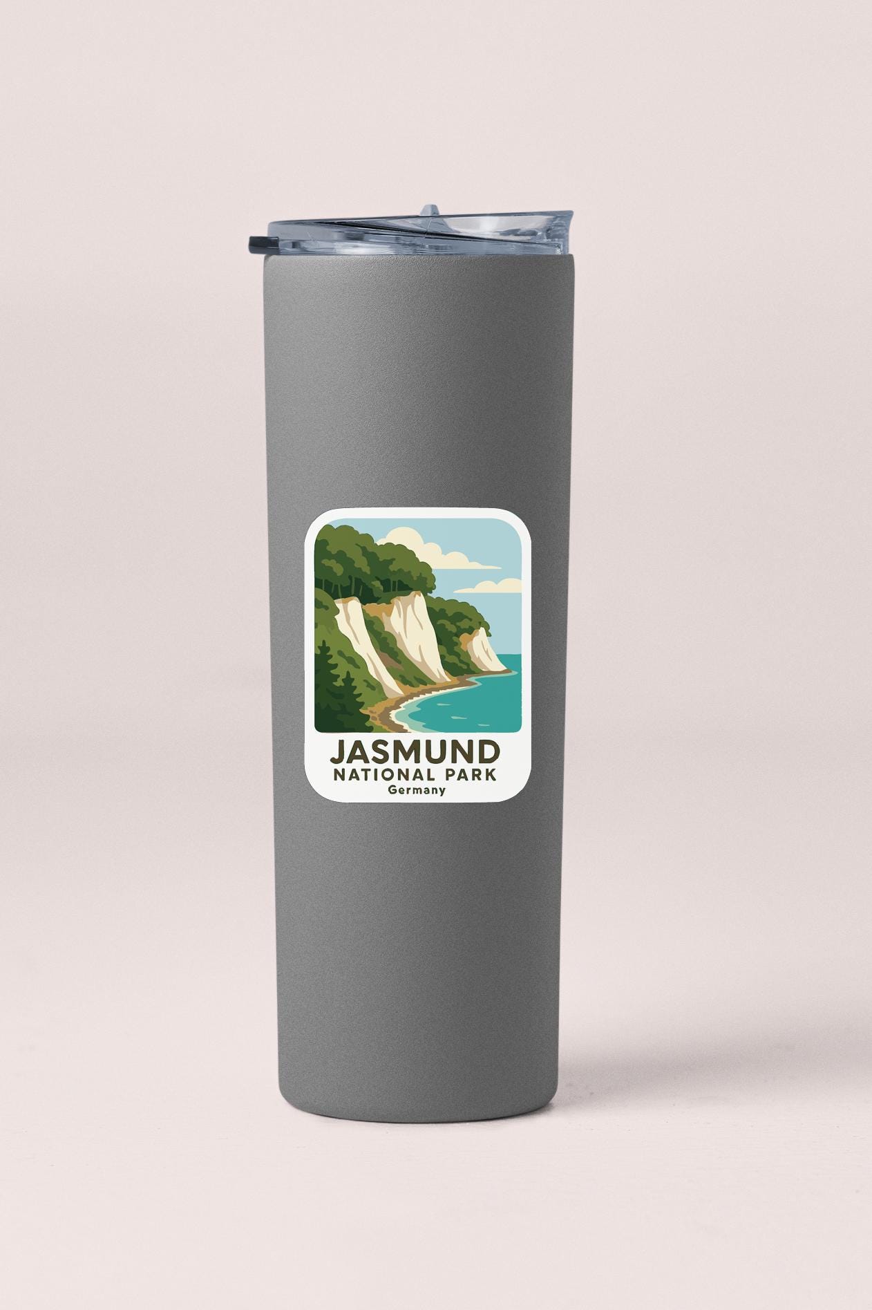 A gray insulated tumbler with a sticker depicting a scenic landscape featuring cliffs and a beach.