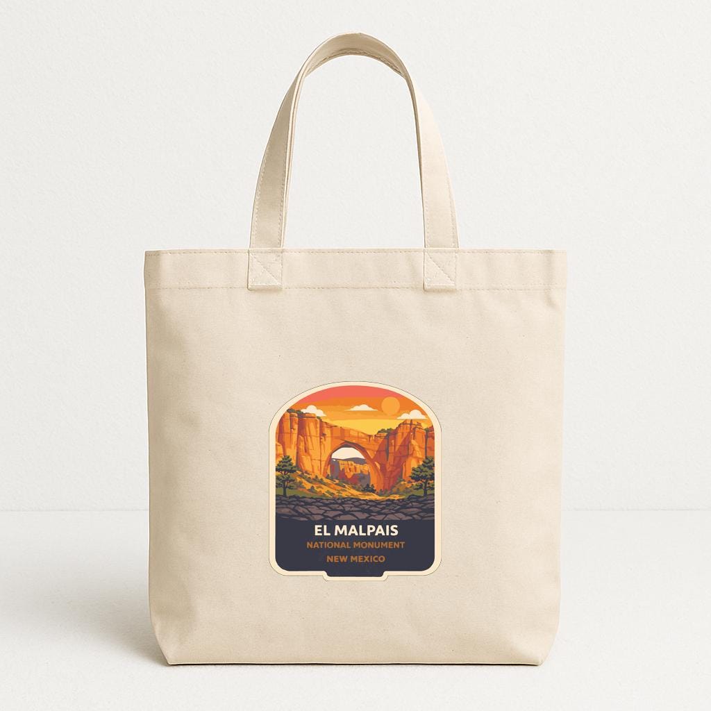 A beige tote bag with a graphic design depicting a scenic landscape with mountains and a sunset.
