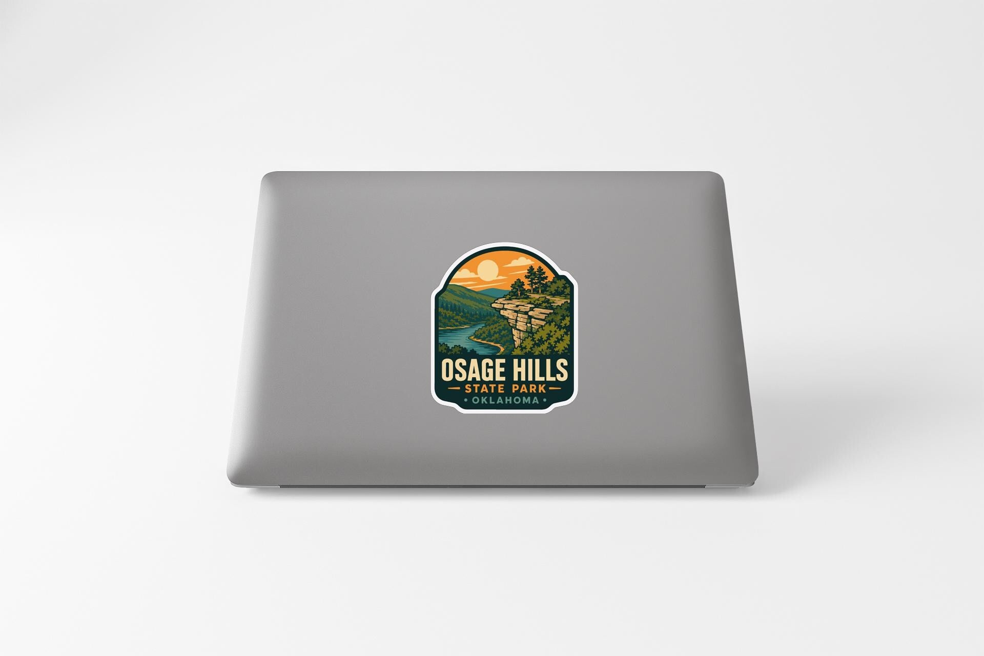 A sticker on the back of a laptop, depicting a scenic landscape with a sunset and mountains.