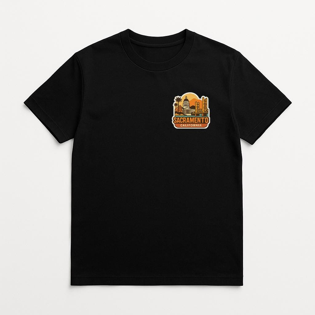 A black t-shirt with a graphic design on the front, depicting a city skyline with the text "SACRAMENTO" prominently displayed.