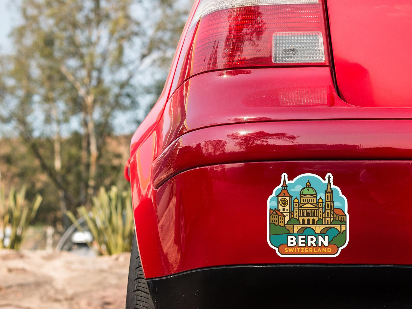 the rear end of a red car with a sticker on it, featuring an illustration of a cityscape with a church.