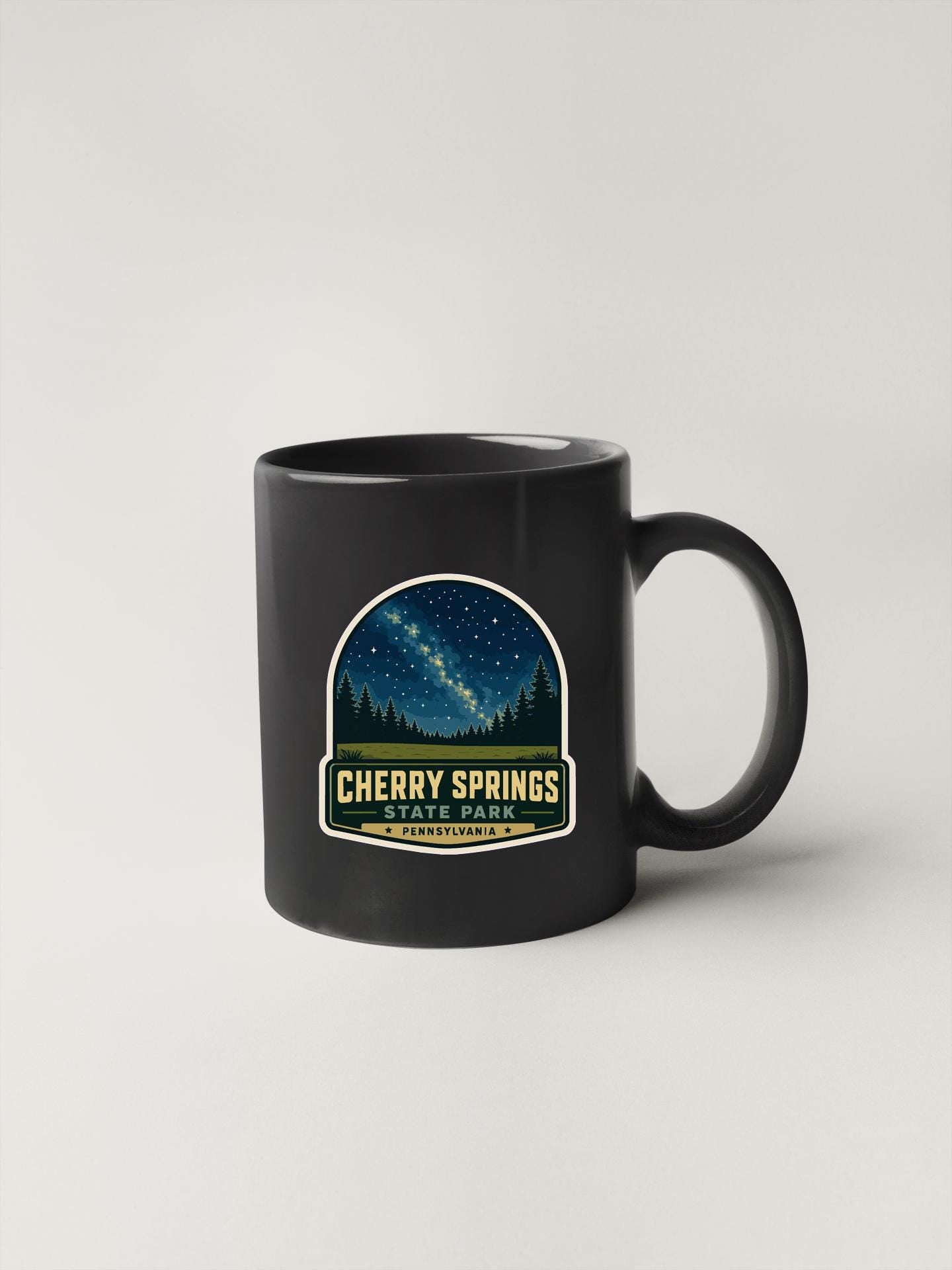 A black coffee mug with a label that says "CHERRY SPRINGS STATE PARK" and features a night sky with stars.
