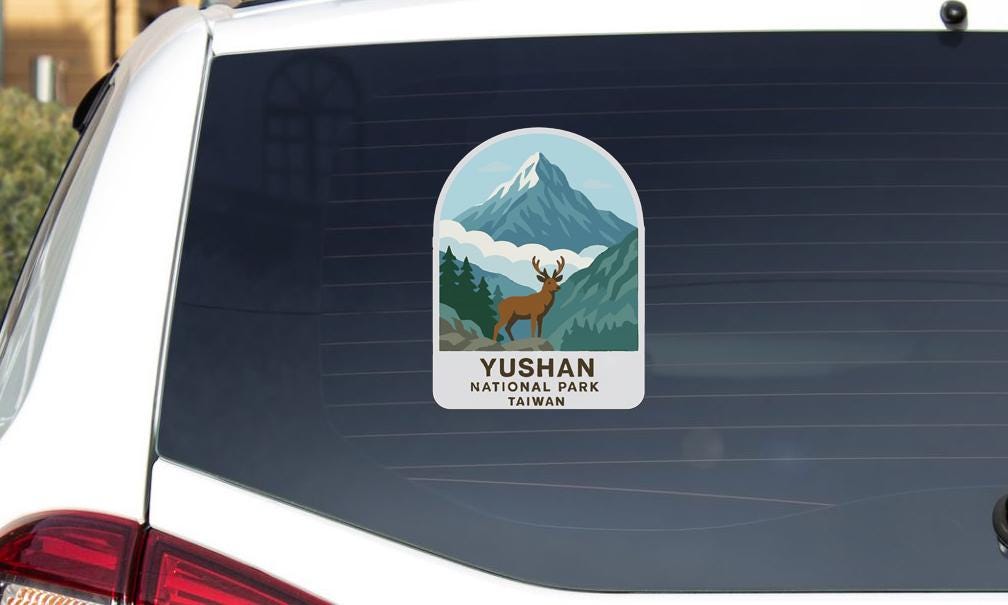 A sticker on the rear window of a car, depicting a mountain landscape with a deer in the foreground.