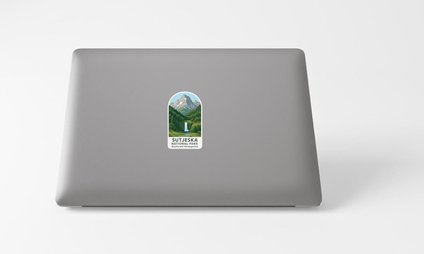 A sticker with a mountain landscape and a waterfall is placed on the back of a laptop computer.