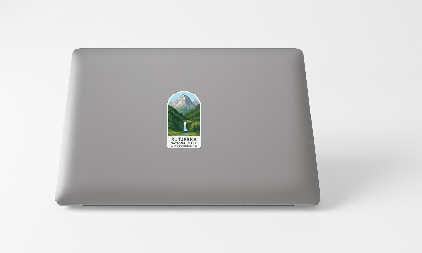 A sticker with a mountain landscape and a waterfall is placed on the back of a laptop computer.
