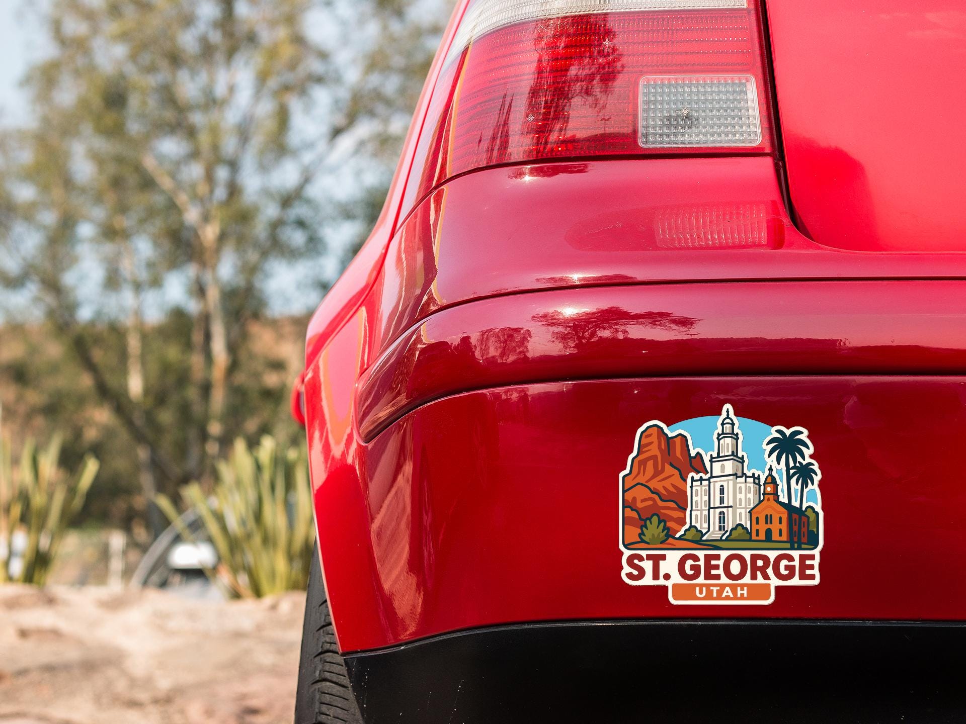 the rear end of a red car with a sticker on the back window that features an illustration of St. George, Utah.