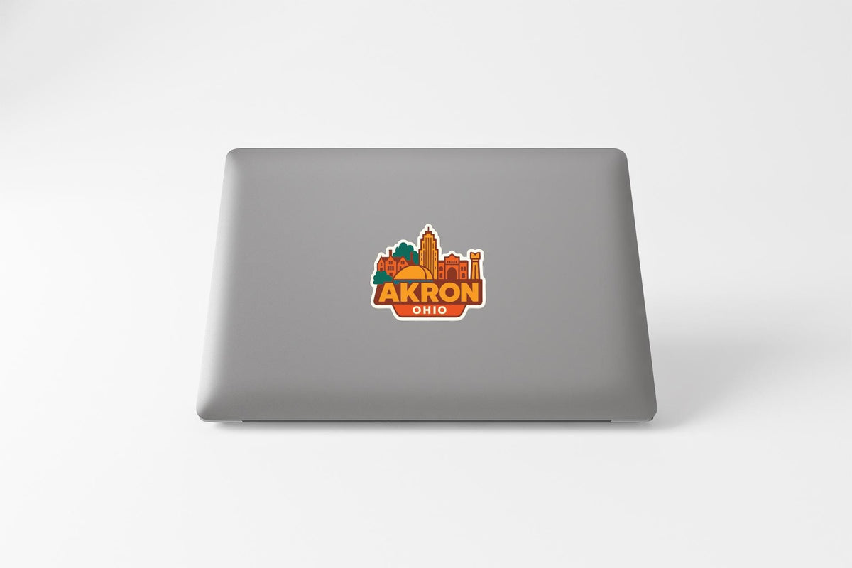 a sticker with a cityscape and the text "AKRON OHIO" on the back of a laptop.