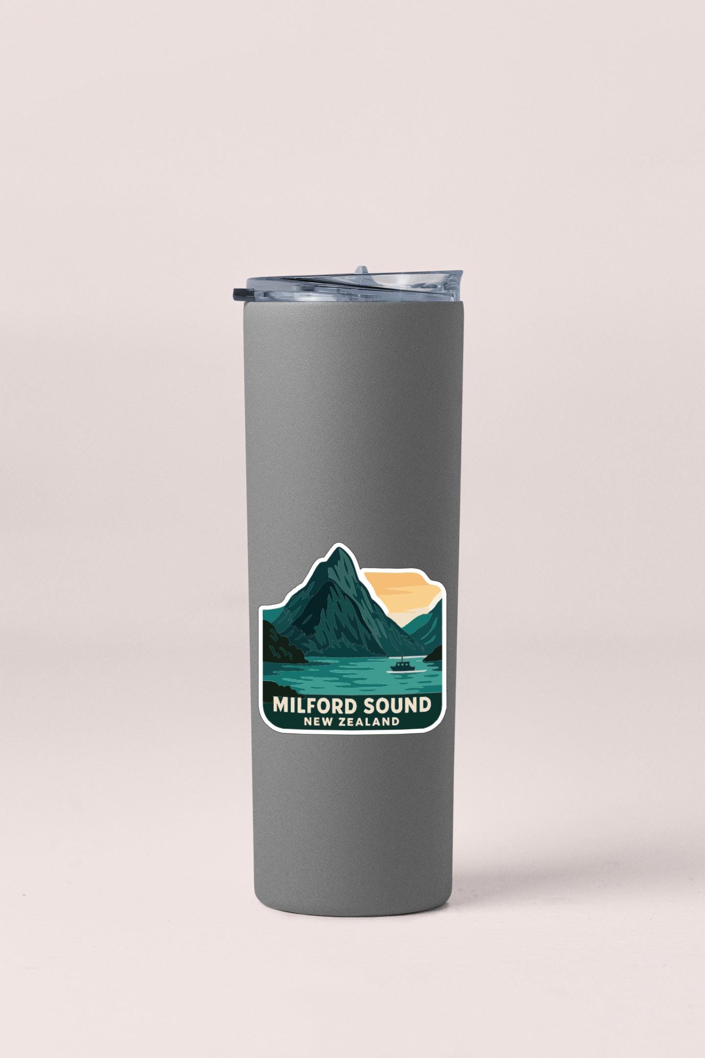 A gray insulated tumbler with a sticker depicting Milford Sound, New Zealand.