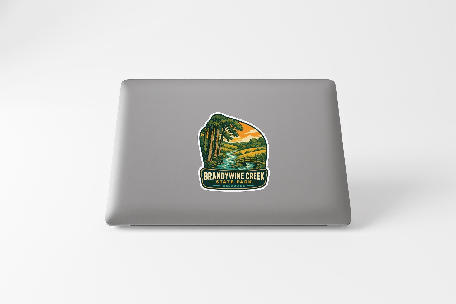 A sticker on the back of a laptop, depicting a scenic landscape with a river and trees.