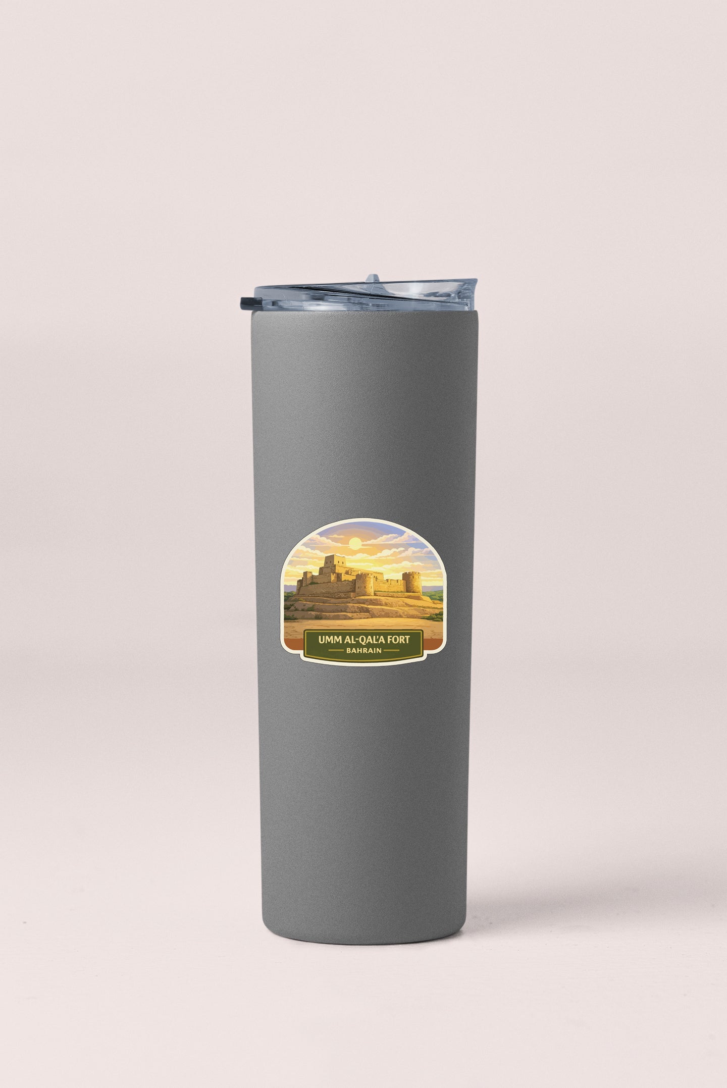 A gray insulated tumbler with a label that reads "UMM AL-QA'A FORT BARCELONA" and features a graphic of a desert landscape with a castle.