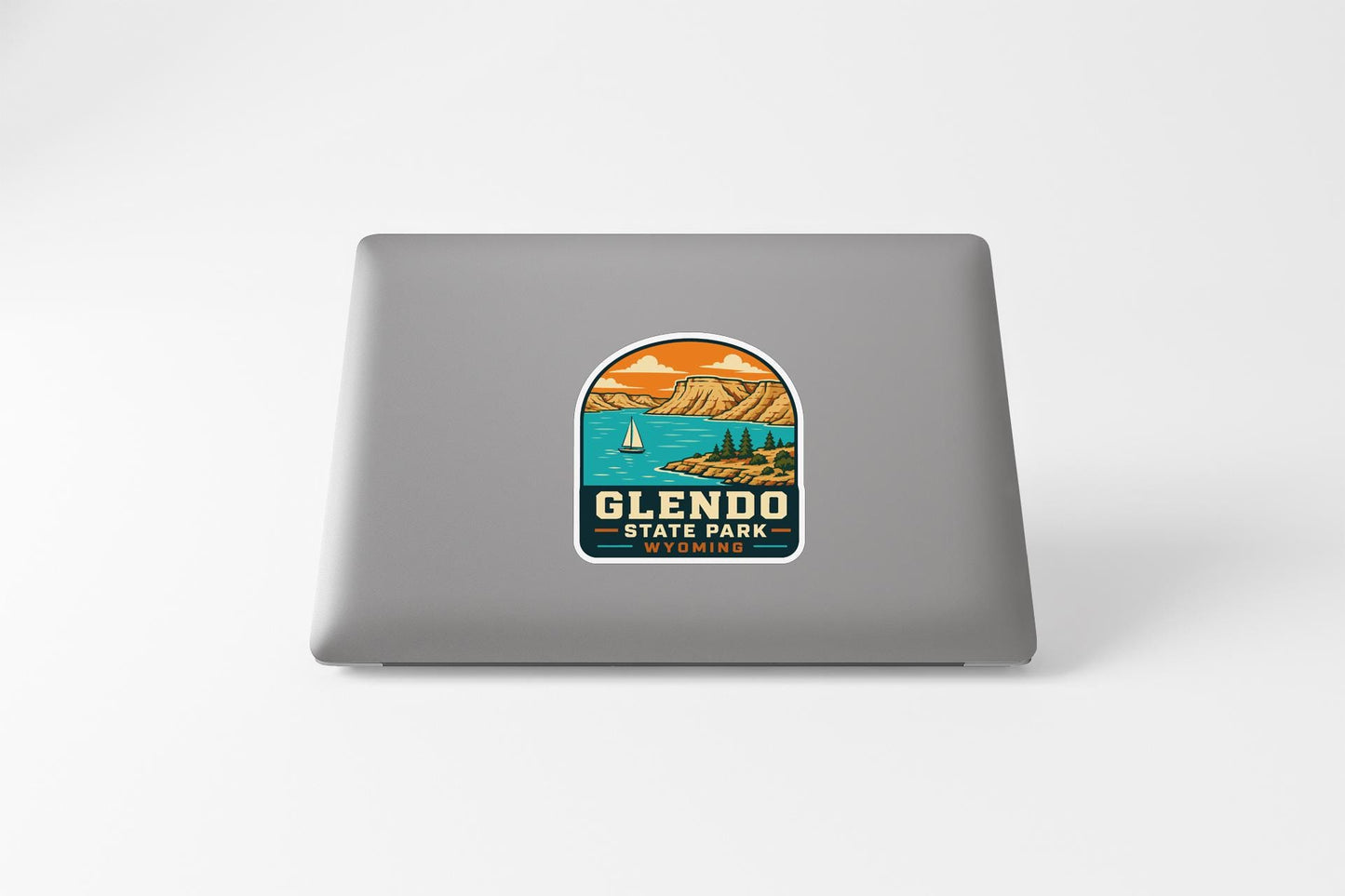 A sticker on the back of a laptop, depicting a scenic landscape with mountains, a lake, and a sailboat.