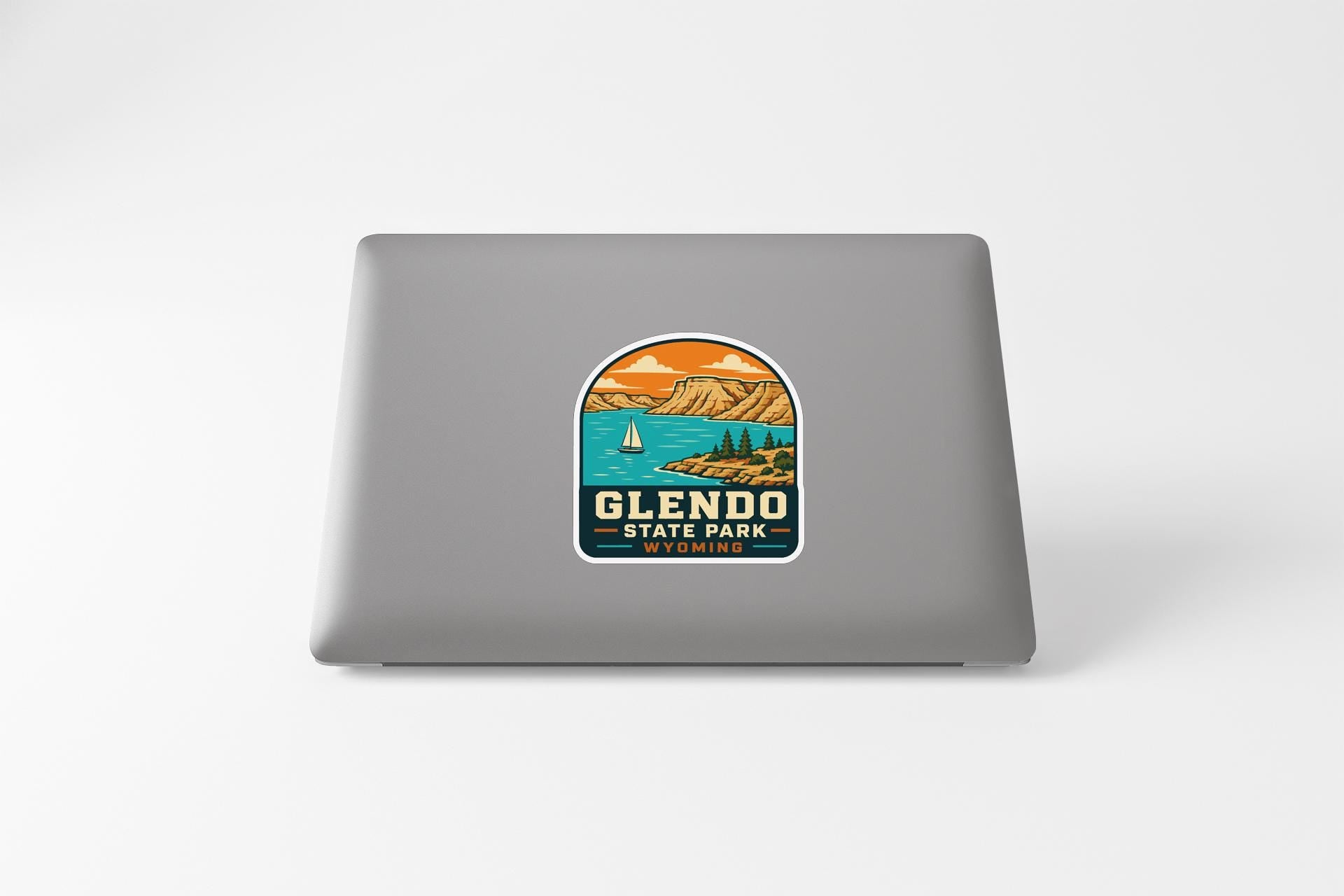 A sticker on the back of a laptop, depicting a scenic landscape with mountains, a lake, and a sailboat.
