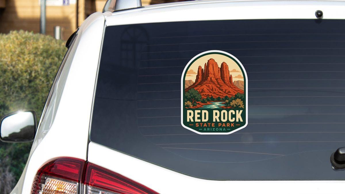 A sticker on the rear window of a white car, depicting the iconic Red Rock State Park in Arizona.